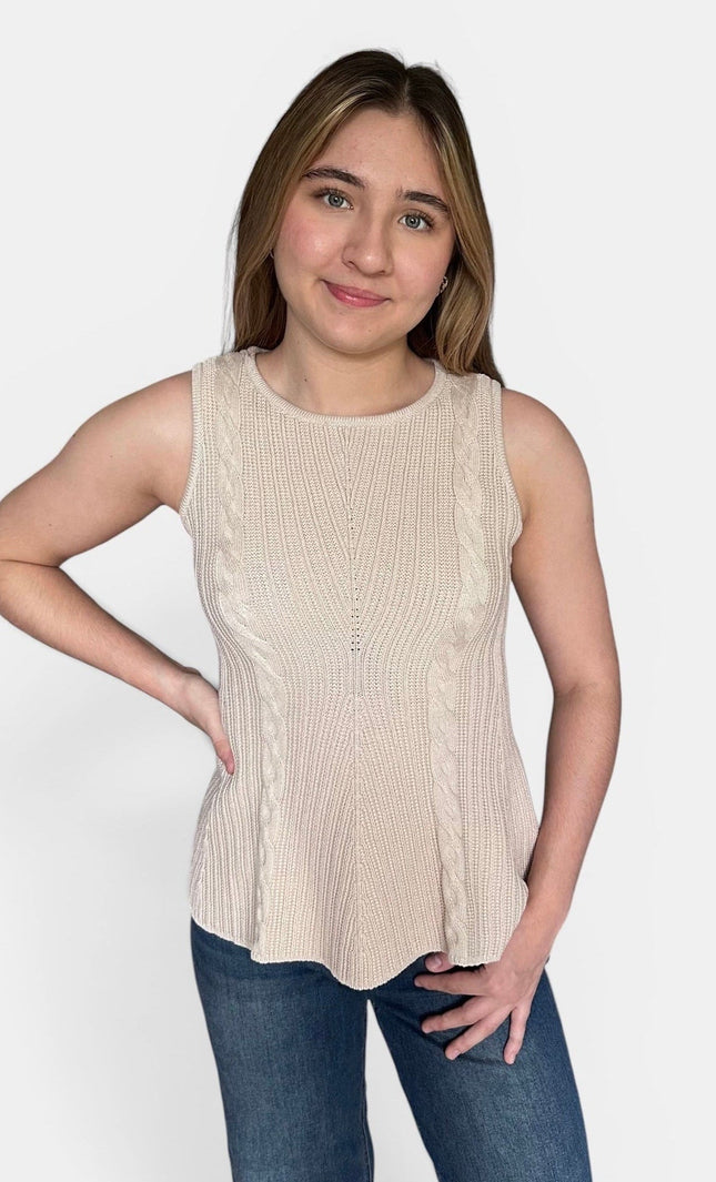 A woman modeling a sleeveless ribbed knit peplum top in a light beige color, paired with blue jeans, against a plain light gray background.