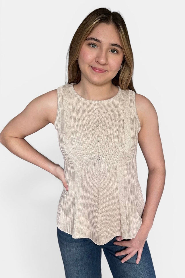A woman modeling a sleeveless ribbed knit peplum top in a light beige color, paired with blue jeans, against a plain light gray background.