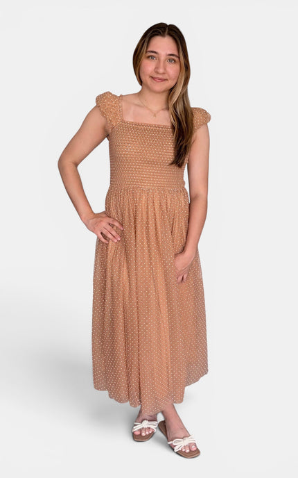 Woman wearing a latte Swiss dot midi dress with a smocked bodice and flutter cap sleeves