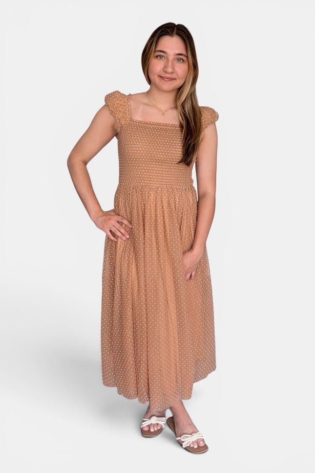 Woman wearing a latte Swiss dot midi dress with a smocked bodice and flutter cap sleeves