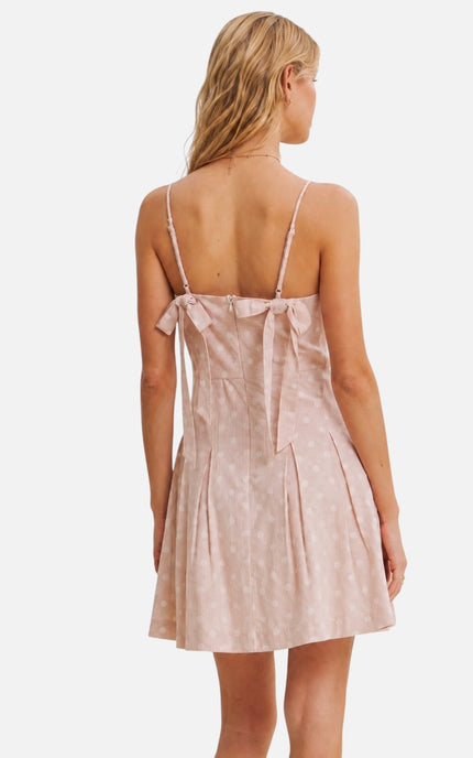 A woman shown from the back wearing a light pink spaghetti-strap dress with a bow detail at the back of the neckline, set against a plain white background.