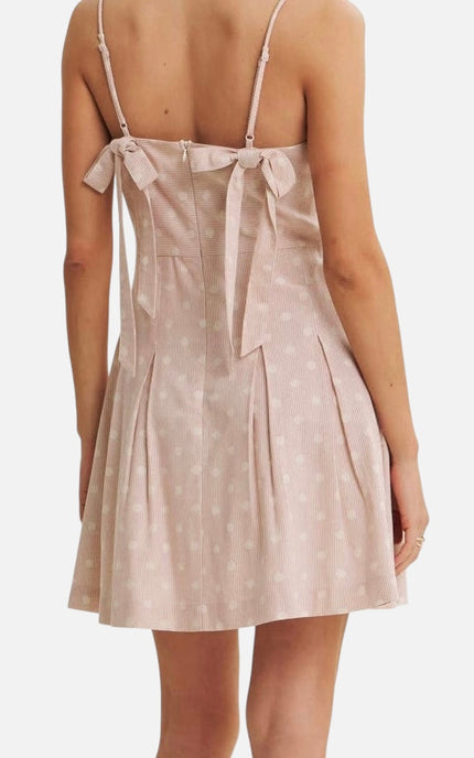 A woman wearing a light pink spaghetti-strap dress with a white polka dot pattern, shown from the back against a plain white background.