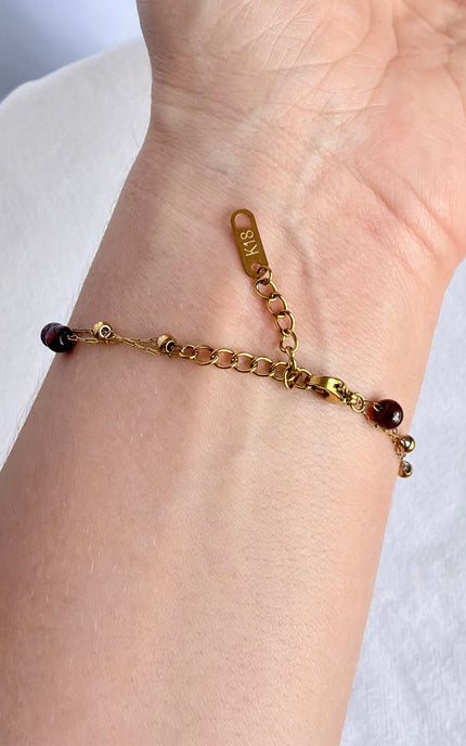 A gold chain bracelet with small dark red beads, shown worn on a person's wrist.