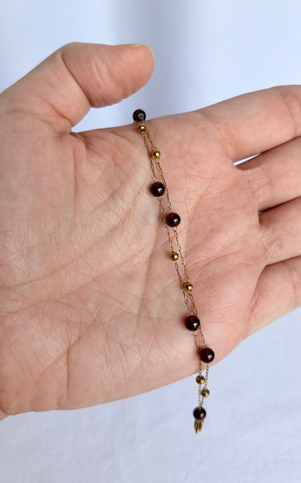 A delicate beaded chain bracelet with dark brown and gold beads, draped across a person's hand to show its scale and design.
