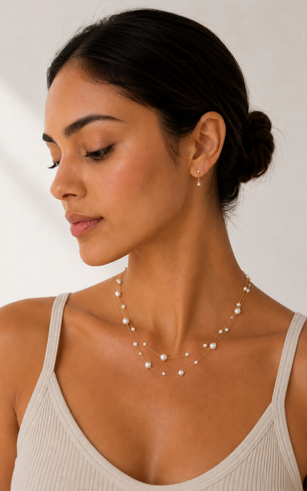 Woman wearing a double strand 18k gold paperclip chain necklace with mixed size imitation pearl stations. The layered necklace rests elegantly along the neckline, adding a timeless, feminine touch to a neutral outfit.