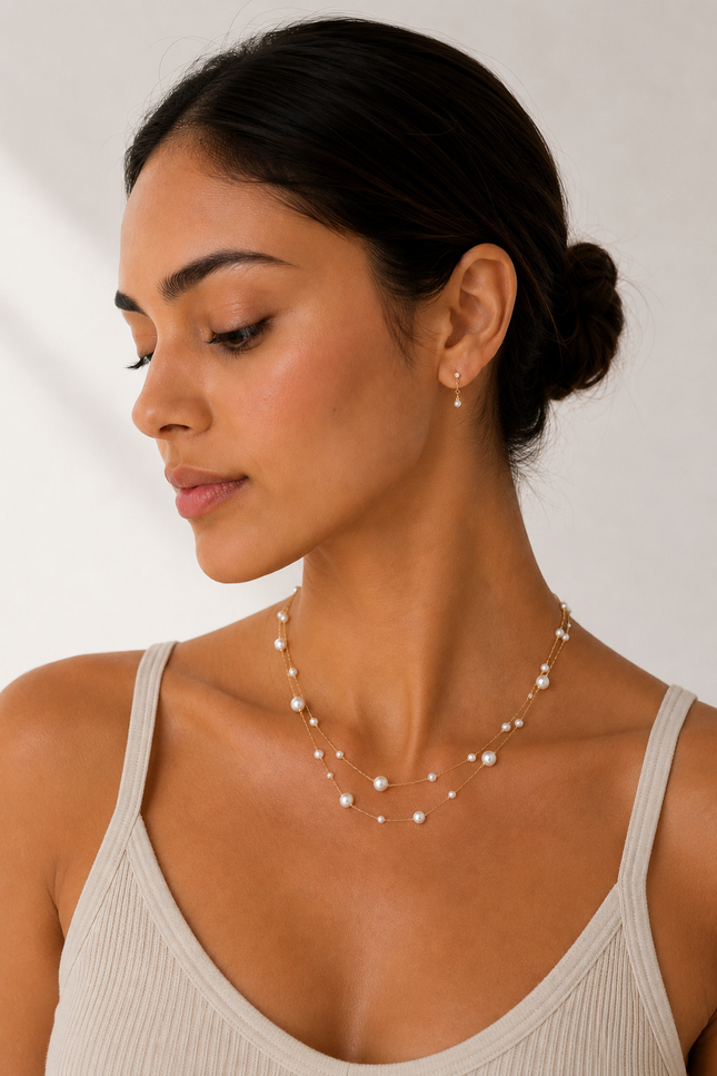 Woman wearing a double strand 18k gold paperclip chain necklace with mixed size imitation pearl stations. The layered necklace rests elegantly along the neckline, adding a timeless, feminine touch to a neutral outfit.