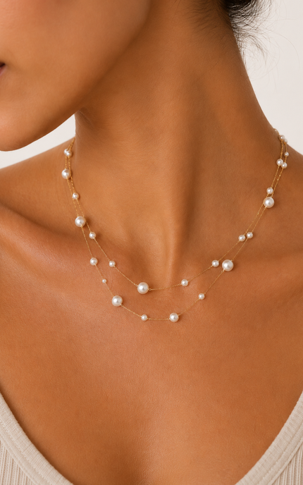 Close up of woman wearing a double strand 18k gold paperclip chain necklace with mixed size imitation pearl stations. The layered necklace rests elegantly along the neckline, adding a timeless, feminine touch to a neutral outfit.