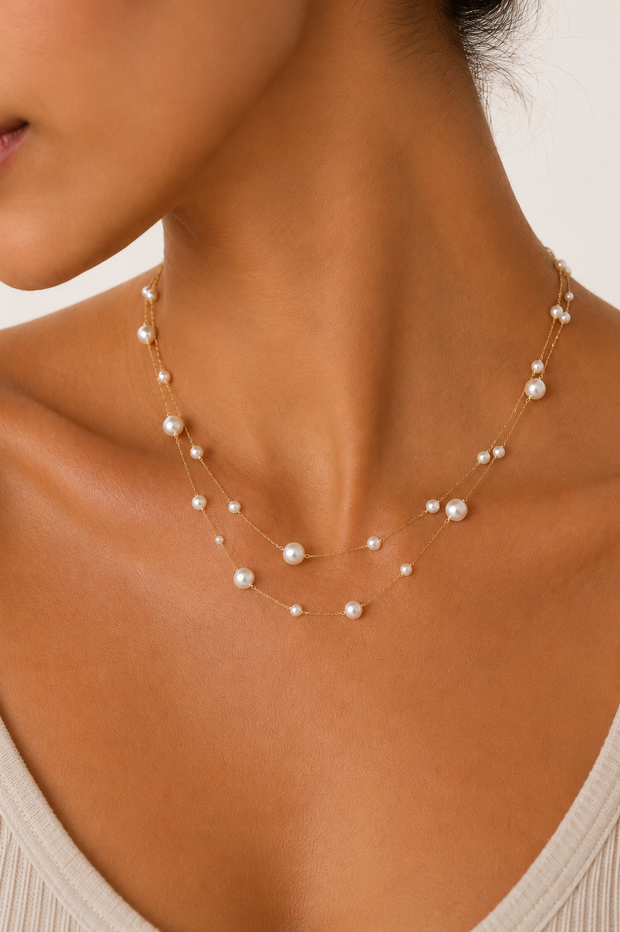 Close up of woman wearing a double strand 18k gold paperclip chain necklace with mixed size imitation pearl stations. The layered necklace rests elegantly along the neckline, adding a timeless, feminine touch to a neutral outfit.