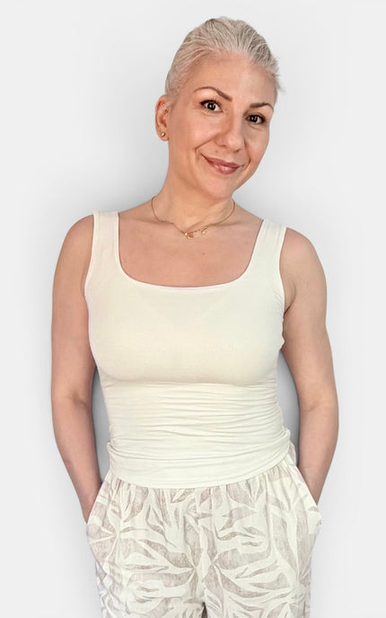 A woman with short platinum blonde hair wearing a cream-colored scoop-neck tank top and matching cream patterned pants, standing against a light gray background.