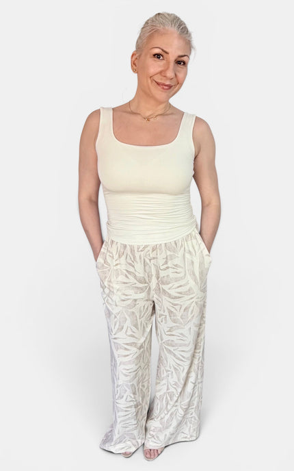 A woman modeling a cream-colored sleeveless top and matching patterned wide-leg pants against a plain light gray background.