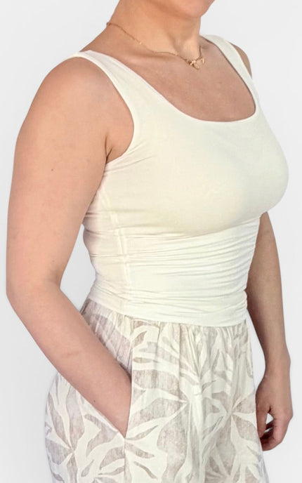 A woman wearing a cream-colored ribbed scoop-neck tank top paired with a matching cream patterned skirt, shown from the chest down against a plain light background.