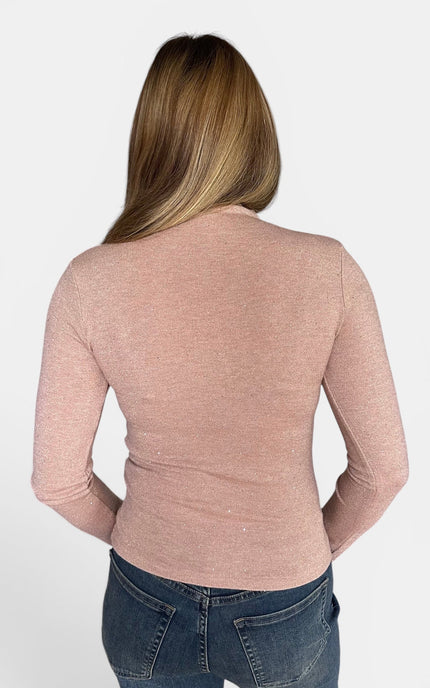 A woman viewed from the back wearing a fitted, long-sleeve dusty rose pink top and dark blue jeans against a plain white background.