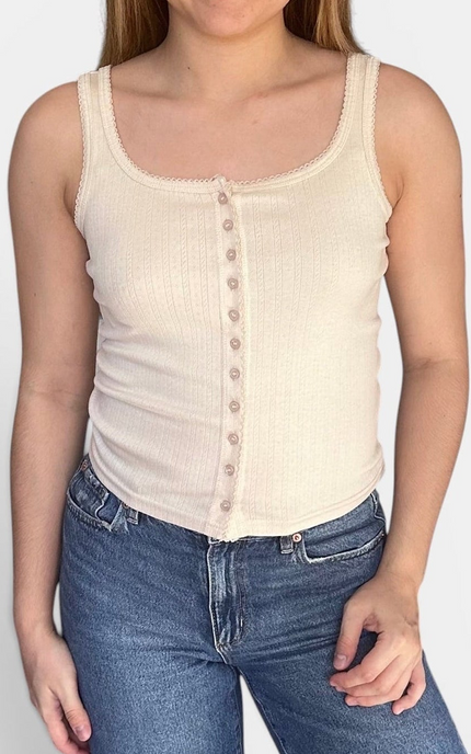 A woman wearing a cream ribbed tank top with a button-down front and blue jeans, cropped from the chin down against a plain light background.