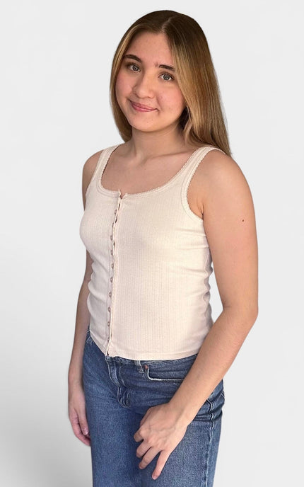 A young woman modeling a ribbed cream-colored tank top with a button-down front, paired with blue jeans, against a plain light gray background.