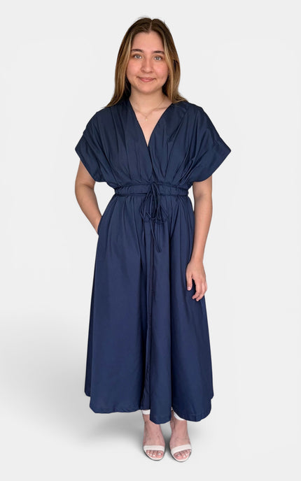 A woman modeling a navy blue maxi dress with short flutter sleeves, a V-neckline, and a self-tie waist belt, set against a plain light gray background.