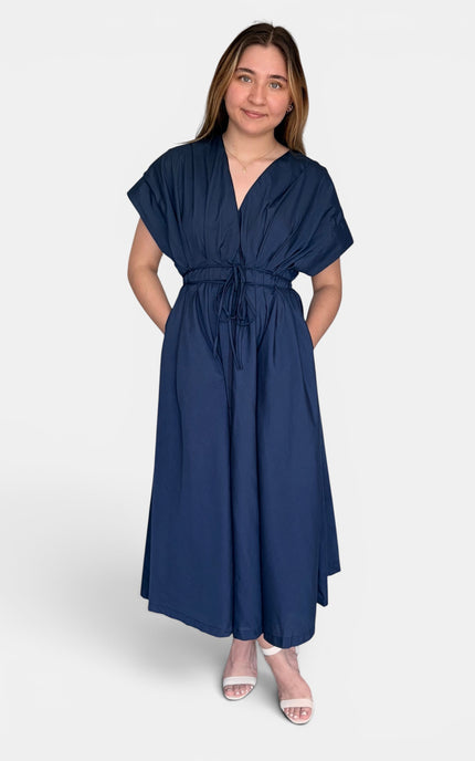 A woman modeling a navy blue maxi dress with short flutter sleeves, a V-neckline, and a self-tie waist belt, photographed against a light gray studio background.