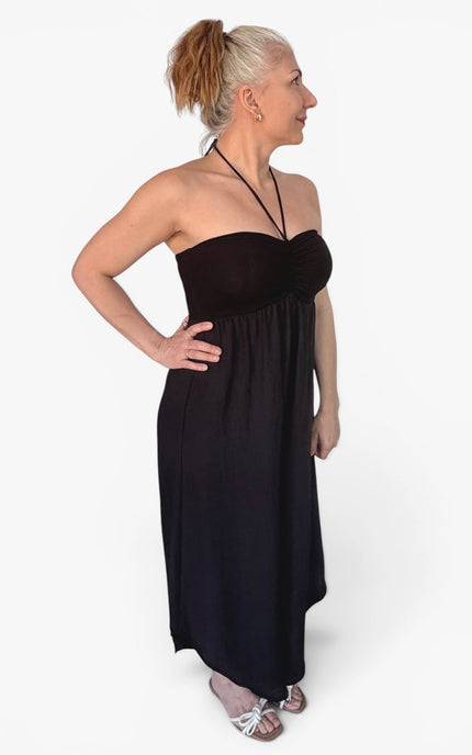 A woman modeling a strapless black maxi dress with a halter-style neckline, standing against a plain white studio background.