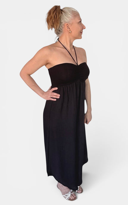 A woman modeling a strapless black maxi dress with a sweetheart neckline and thin halter-style straps, shown against a plain light gray studio background.