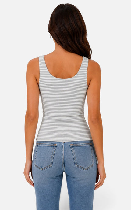A woman viewed from the back wearing a fitted sleeveless tank top with thin horizontal gray stripes on a white base, paired with light blue jeans, against a light gray studio background.