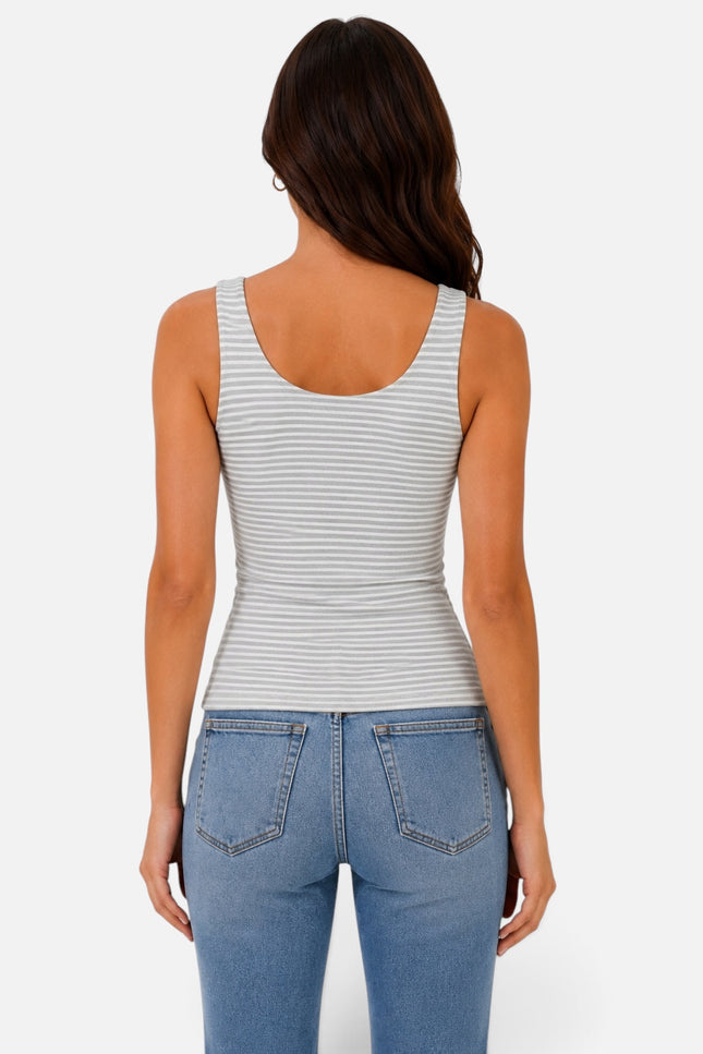 A woman viewed from the back wearing a fitted sleeveless tank top with thin horizontal gray stripes on a white base, paired with light blue jeans, against a light gray studio background.