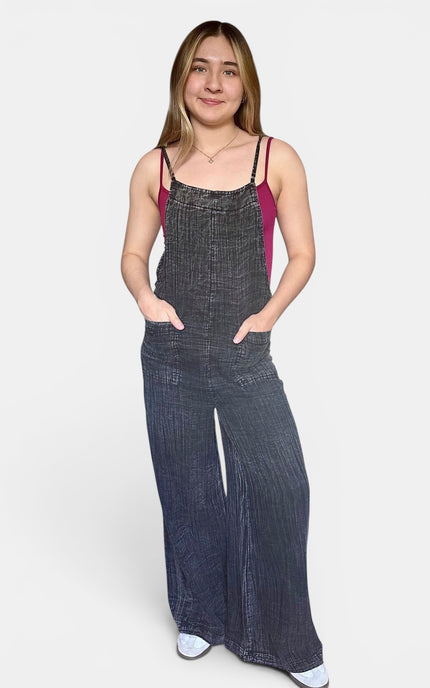 Woman wearing a black sleeveless wide leg cotton jumpsuit with adjustable straps and side pockets.