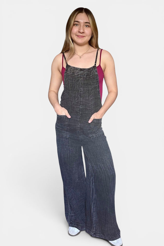 Woman wearing a black sleeveless wide leg cotton jumpsuit with adjustable straps and side pockets.