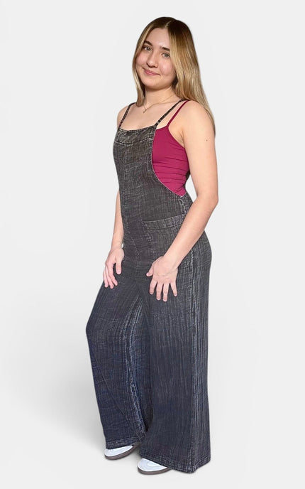  Side view of casual black sleeveless jumpsuit with a loose wide leg silhouette styled for warm weather.