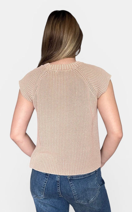 A woman viewed from the back wearing a beige ribbed knit short-sleeve top and blue jeans against a light gray studio background.
