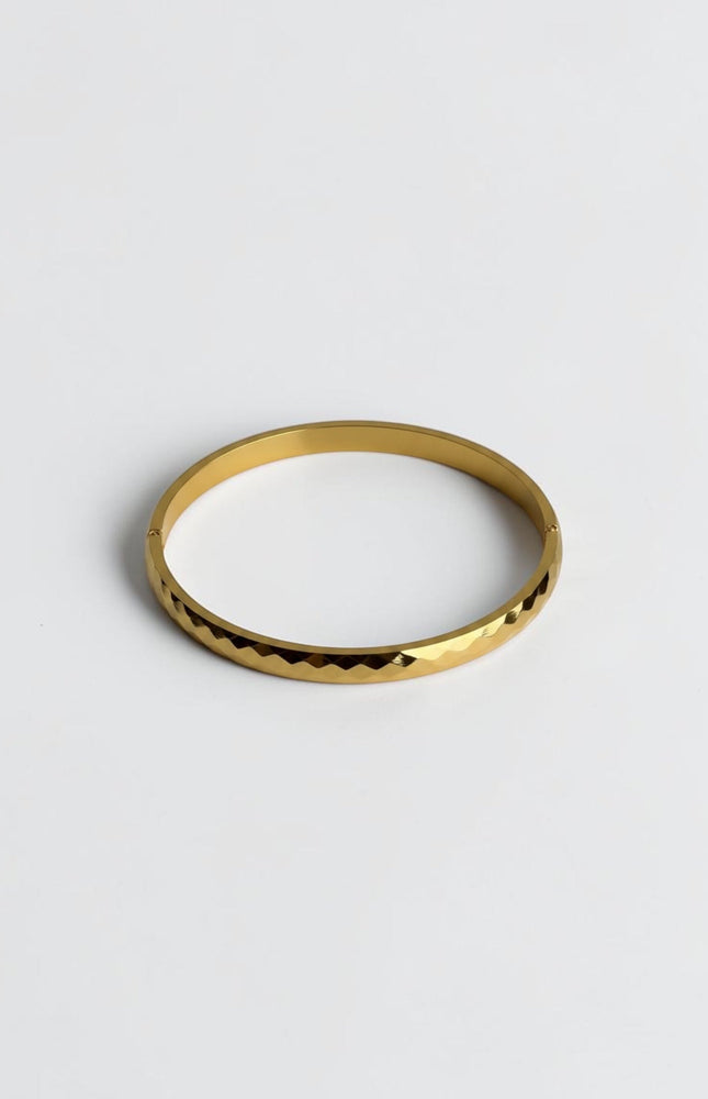 Close-up of a polished gold geometric bangle showing light-reflecting edges