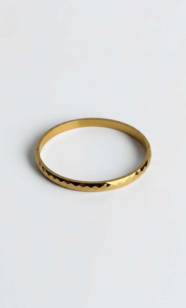 Close-up of a polished gold geometric bangle showing light-reflecting edges