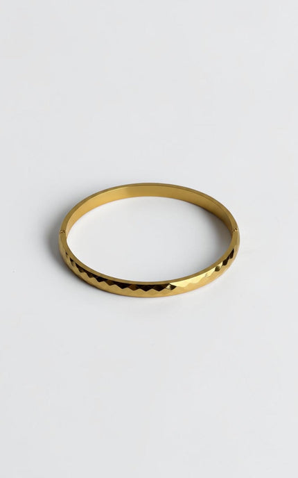 Close-up of a polished gold geometric bangle showing light-reflecting edges