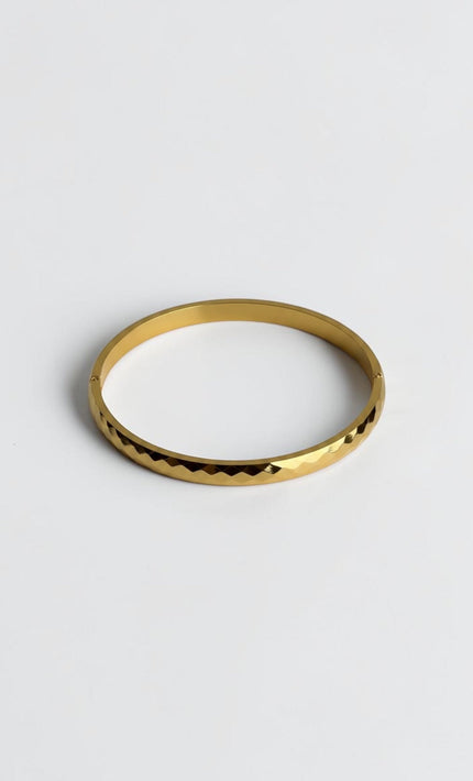 Close-up of a polished gold geometric bangle showing light-reflecting edges