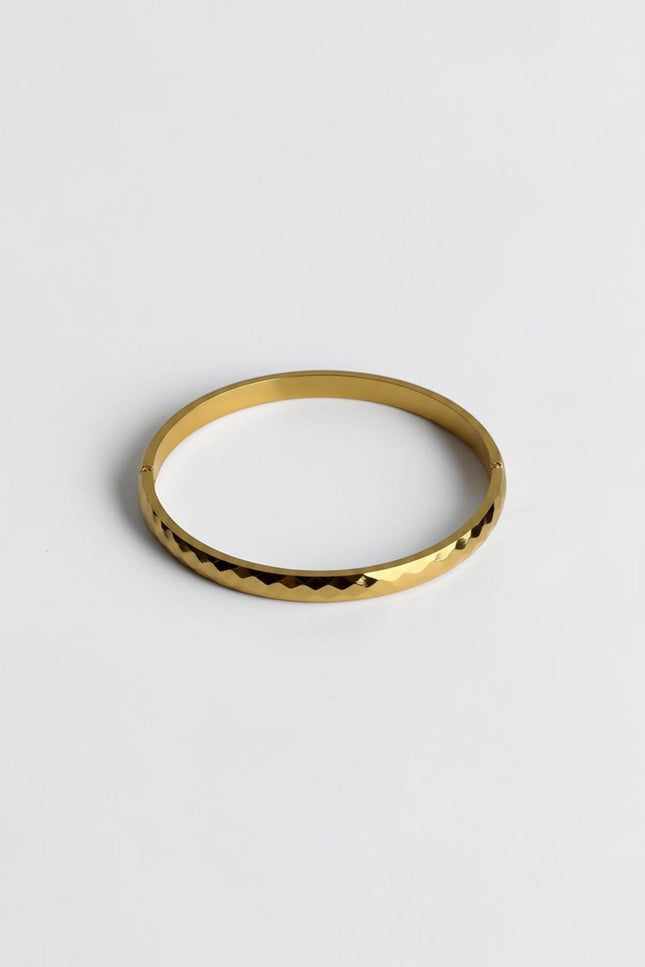 Close-up of a polished gold geometric bangle showing light-reflecting edges