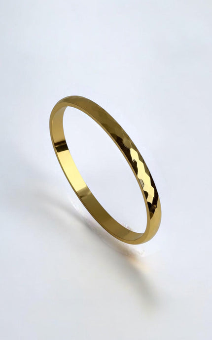 Close-up of a polished gold geometric bangle showing light-reflecting edges