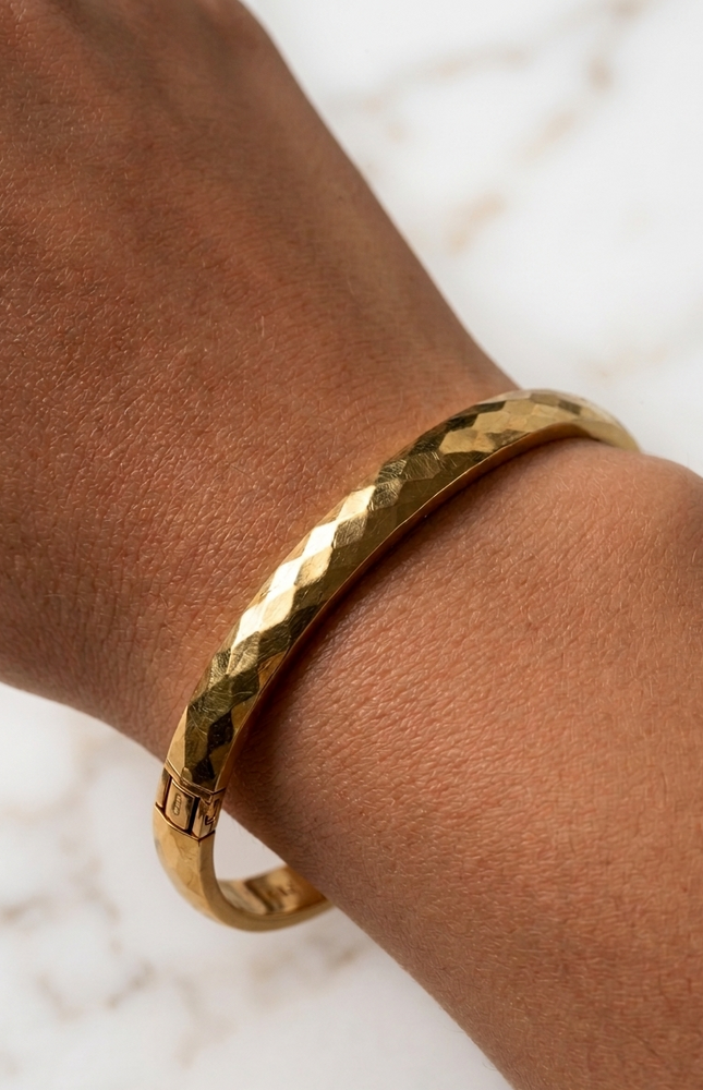 Faceted gold bangle bracelet on a woman’s wrist in natural sunlight