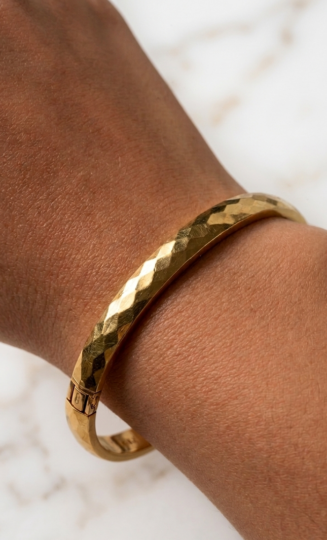 Faceted gold bangle bracelet on a woman’s wrist in natural sunlight