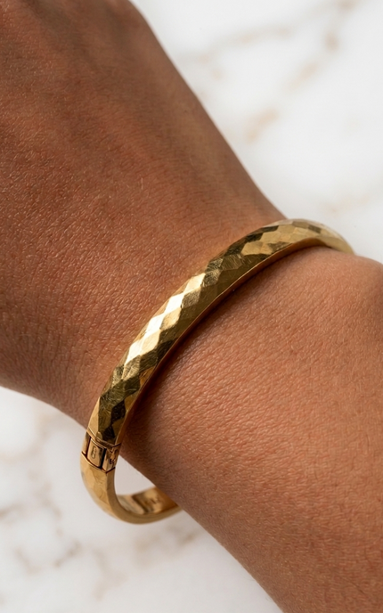 Faceted gold bangle bracelet on a woman’s wrist in natural sunlight
