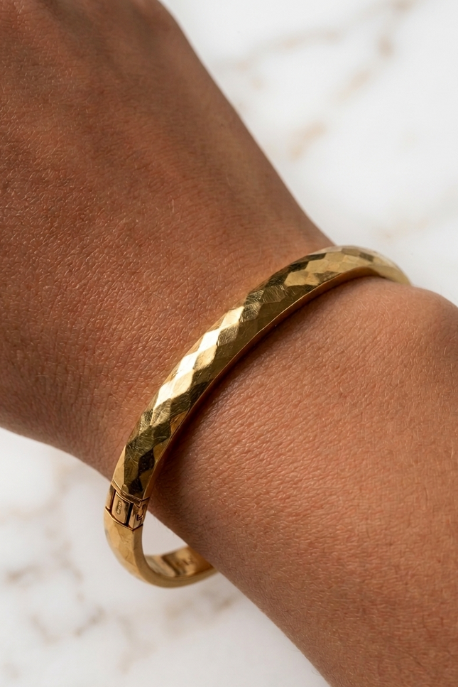Faceted gold bangle bracelet on a woman’s wrist in natural sunlight