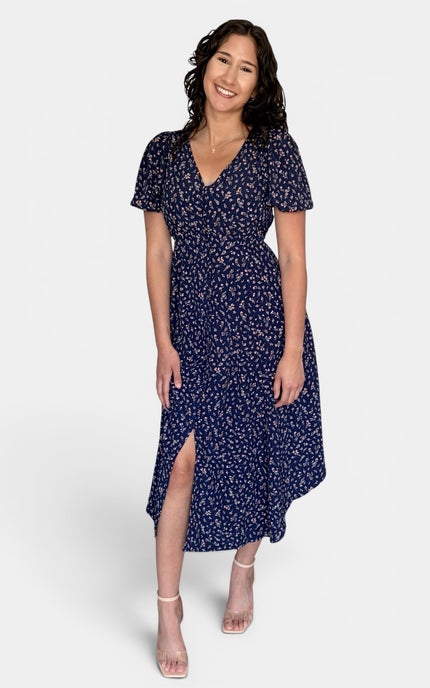 Model wearing a floral V-neck midi dress with short puff sleeves, button-front detail, and side pockets.