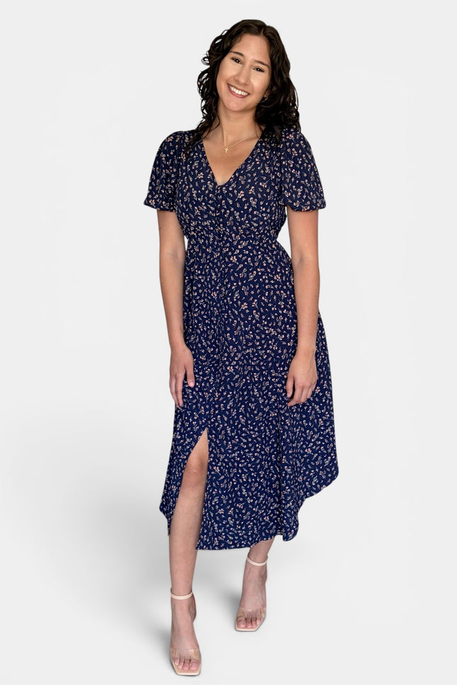 Model wearing a floral V-neck midi dress with short puff sleeves, button-front detail, and side pockets.