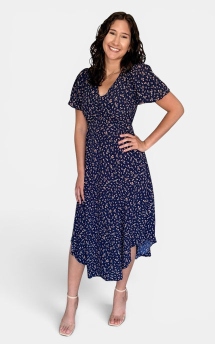 Model wearing a floral V-neck midi dress with short puff sleeves, button-front detail, and side pockets.