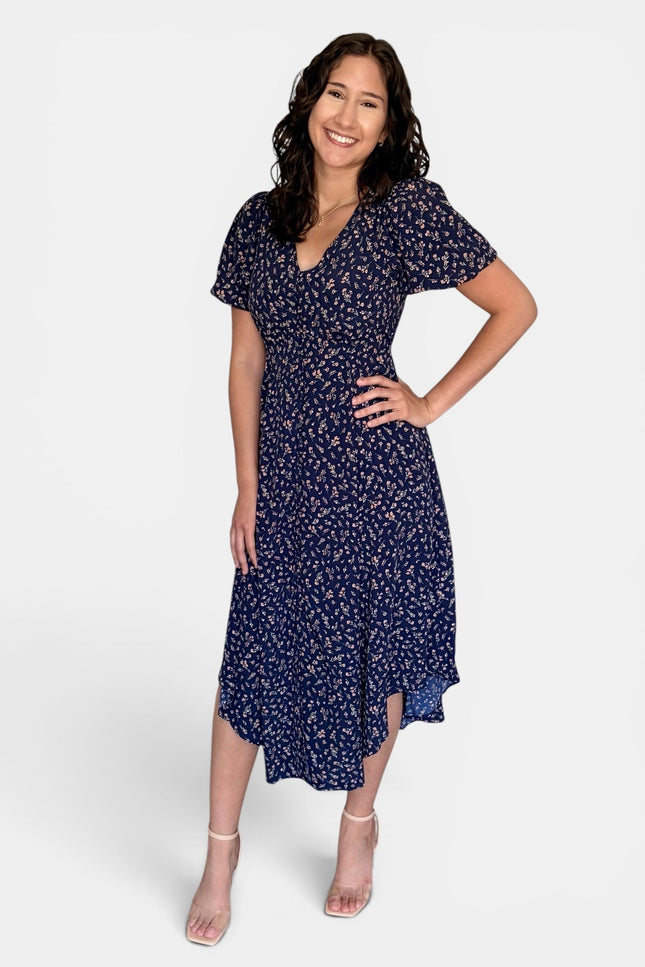 Model wearing a floral V-neck midi dress with short puff sleeves, button-front detail, and side pockets.