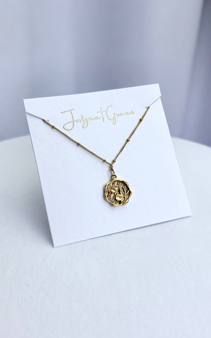 An etched floral cameo coin necklace arranged on a clean boutique display card, showcasing the full pendant face and the tarnish-resistant satellite chain.