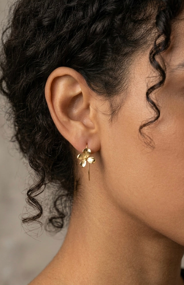 Close-up lifestyle photo of a model wearing the gold 3D flower earring, showing how the delicate floral charm hangs gracefully from its hook wire.