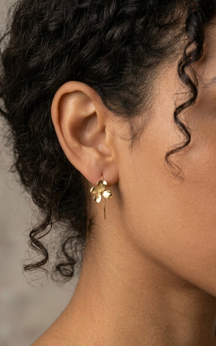 Close-up lifestyle photo of a model wearing the gold 3D flower earring, showing how the delicate floral charm hangs gracefully from its hook wire.