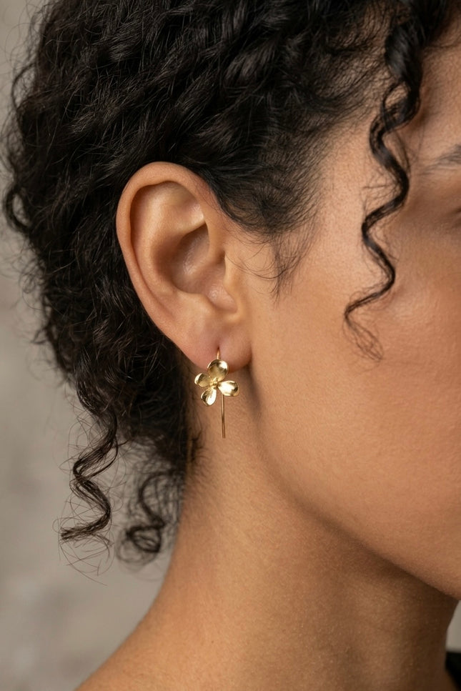 Close-up lifestyle photo of a model wearing the gold 3D flower earring, showing how the delicate floral charm hangs gracefully from its hook wire.