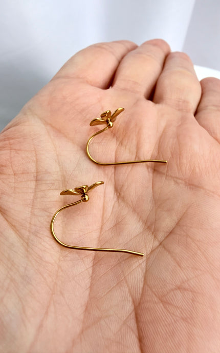 A handheld close-up of the gold Flower Drop Hook Earrings flipped over in the palm of a hand, showcasing the smooth, polished back of the 3D flower charms and the clean, curved line of the open hook wires.