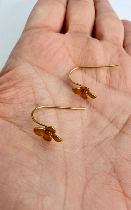 A casual, handheld photo of the gold Flower Drop Hook Earrings cradled in a palm under soft, warm lighting, emphasizing the lightweight, effortless style and radiant shine of the tarnish-free pieces.