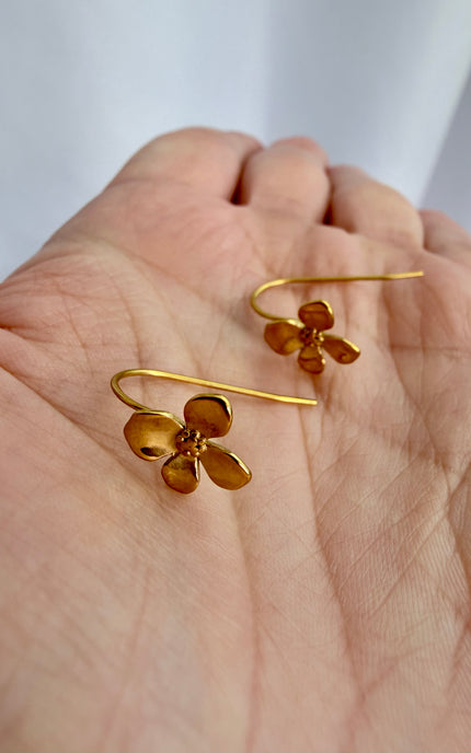 A close up handheld photo of the gold Flower Drop Hook Earrings cradled in a palm under soft, warm lighting, emphasizing the lightweight, effortless style and radiant shine of the tarnish-free pieces.