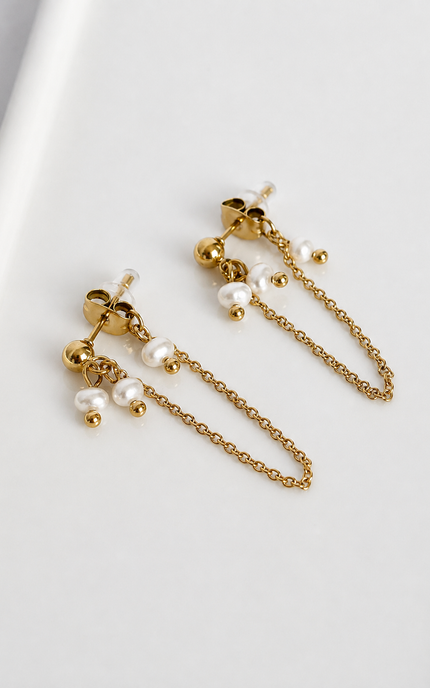 A pair of gold-toned dangle earrings with small white pearl-like beads and chain details, photographed on a clean white surface.